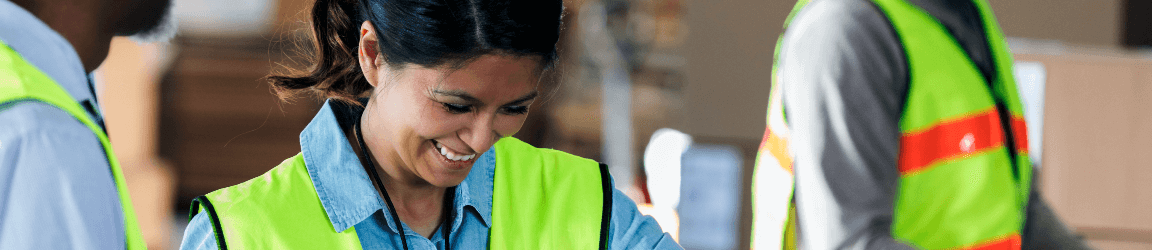 A woman warehouse worker wearing a neon vest at work smiling