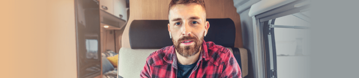 A young bearded man wearing ear pods and red flannel shirt faces the camera during a virtual interview.