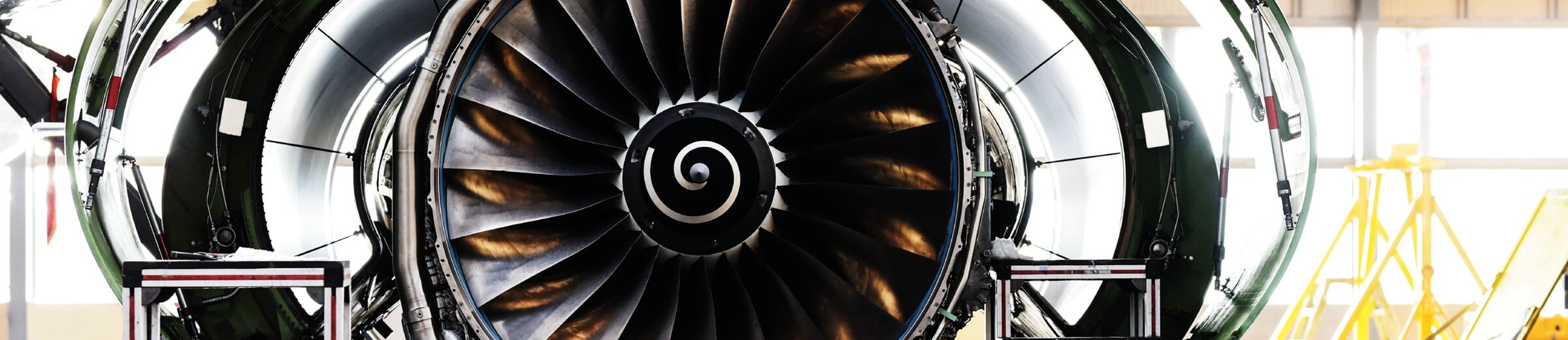 A close-up view of a jet engine reveals its intricate design and metallic surfaces, capturing the essence of modern aviation technology. The engine is partially disassembled, exposing the inner blades that gleam with a polished finish. In the background, a well-lit hangar sets the stage for maintenance or inspection.