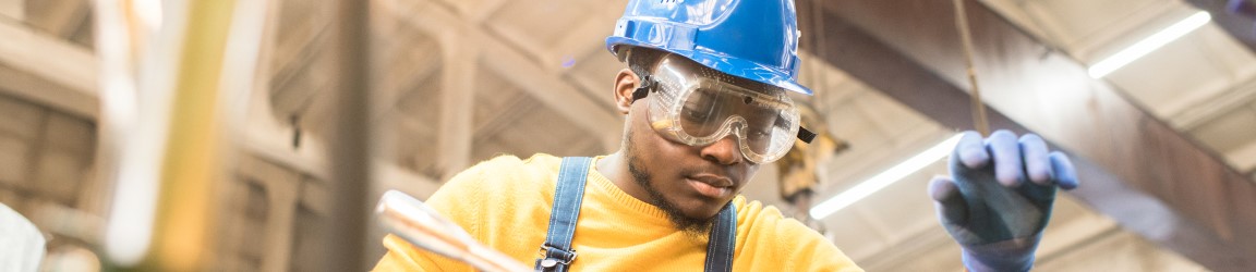 A maintenance worker in overalls and a blue hard hat works on something with his hands