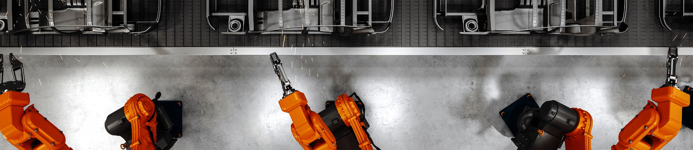 A top-down view of an industrial setting featuring three bright orange industrial robots with black bases, positioned on a grey floor. Each robot is equipped with different tools at their ends, suggesting specialized functions. Above them, there’s a complex assembly of mechanical components, including gears and conveyors, indicative of a modern automated manufacturing or assembly line. The metallic machinery reflects the ambient light, highlighting the advanced technological environment.
