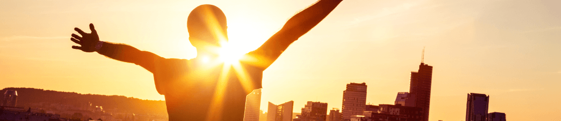 Une personne regarde l'horizon d'une ville avec ses bras tendus pendant le lever du soleil. 