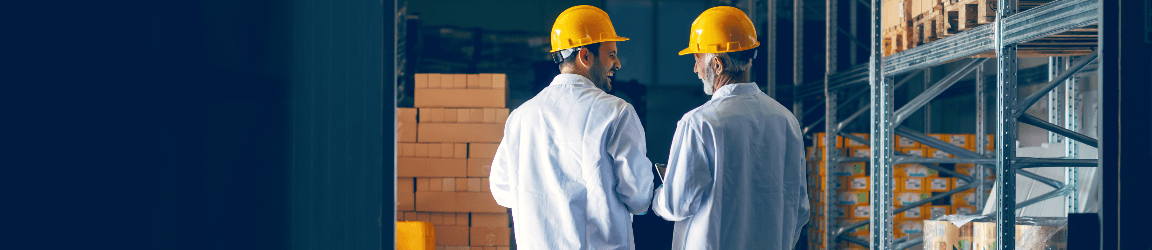 Two men inside a warehouse wearing yellow hardhats