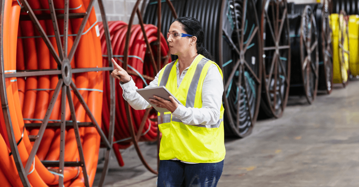 A woman in a reflective vest examines equipment on a work site.
