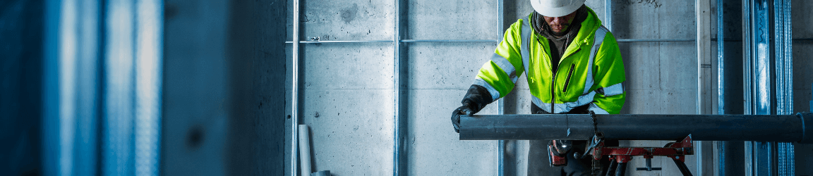 A worker wearing a reflective vest and hard hat works at a table saw on a job site.