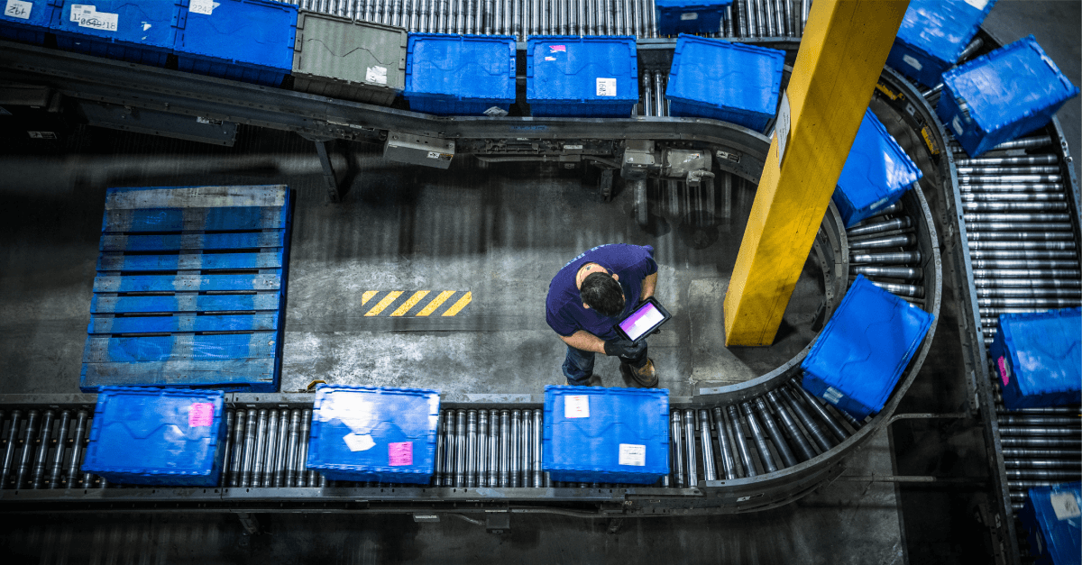 An overhead shot of a worker inspecting a conveyor belt filled with blue boxes