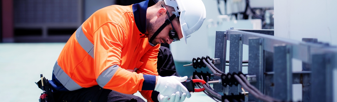 Industrial electrician working on rooftop electrical system maintenance at a commercial facility.
