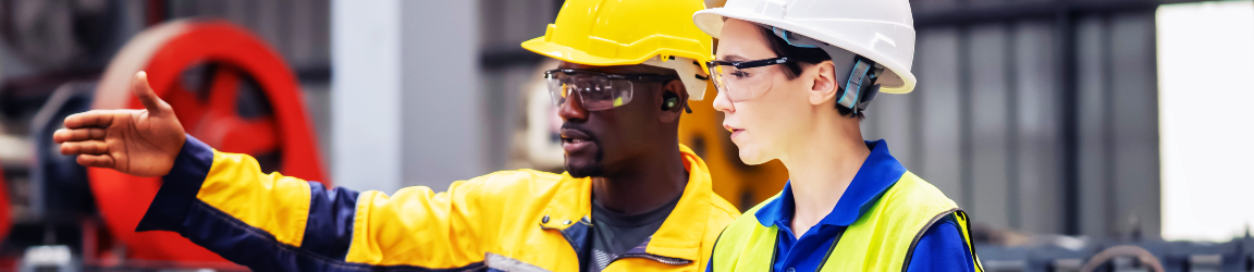Industrial maintenance career concept: two industrial workers inspect machinery and discuss workflow on a production line, highlighting teamwork, troubleshooting and hands-on equipment maintenance in a manufacturing environment.