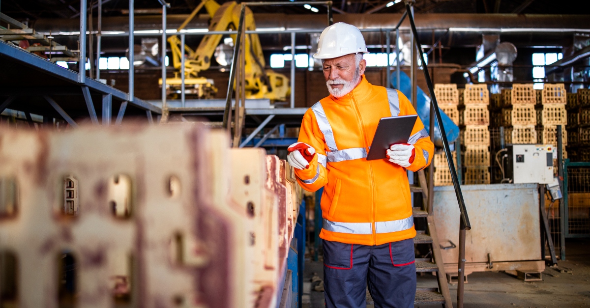 Manufacturing worker reviewing equipment data on a tablet inside a factory, highlighting staffing challenges and the skilled labor shortage in modern manufacturing environments.