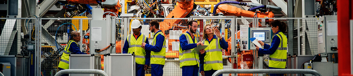 Manufacturing workers in yellow reflective vests work on a production floor 