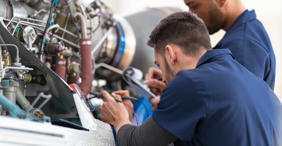 Aircraft maintenance technicians perform diagnostics and inspections on a jet engine using testing equipment and technical documentation. Skilled trades professionals work together on aircraft maintenance and repair tasks in an aviation maintenance facility.