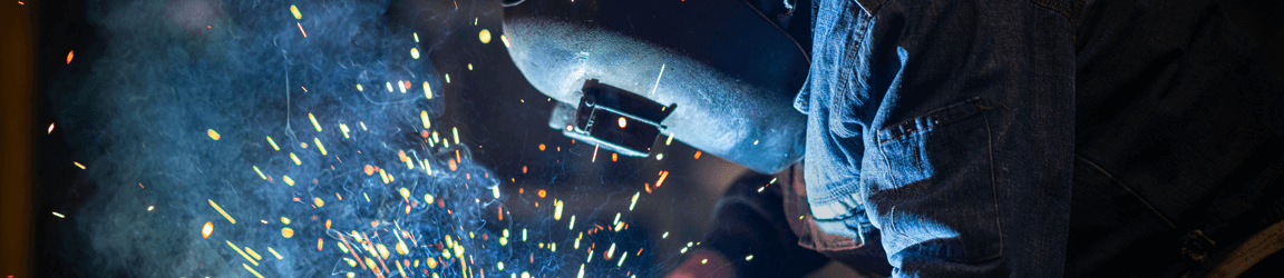 A welder wearing a metal face shield works as sparks fly