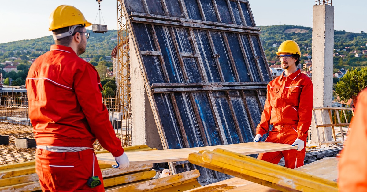 Two construction workers wearing  yellow hard hats and safety vests, move materials through a data center construction site. 