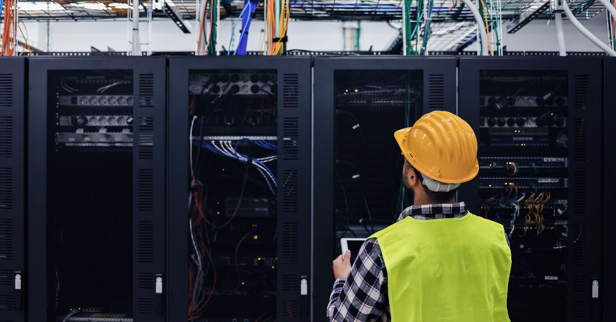 Skilled technician working on data center construction while monitoring servers on a tablet.