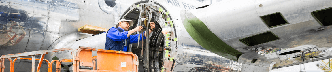 Un mécanicien d'aéronef travaille sur un moteur d'avion dans un hangar d'avion. Il porte une chemise bleue, un gilet et un casque.