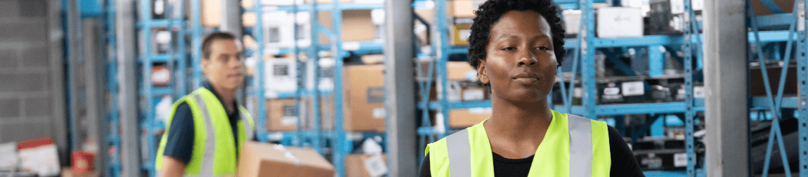 One worker in a fluorescent vest in the background looks at another worker in a fluorescent vest in the foreground