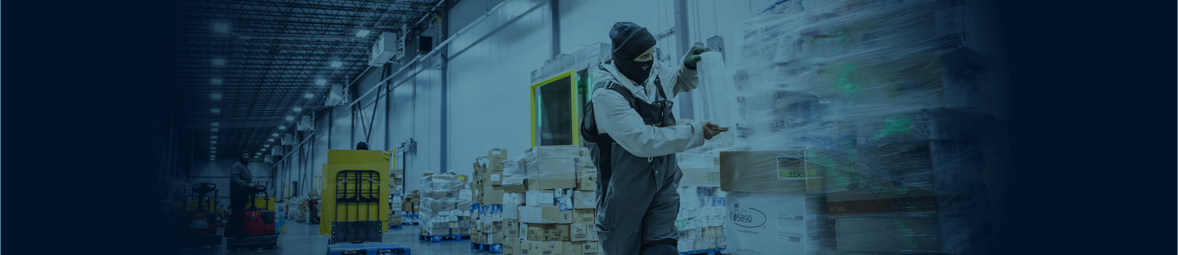 A worker in a warehouse, wearing a mask and winter cap, moves a product.