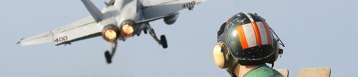 Crewman looking up at military aircraft in the sky.
