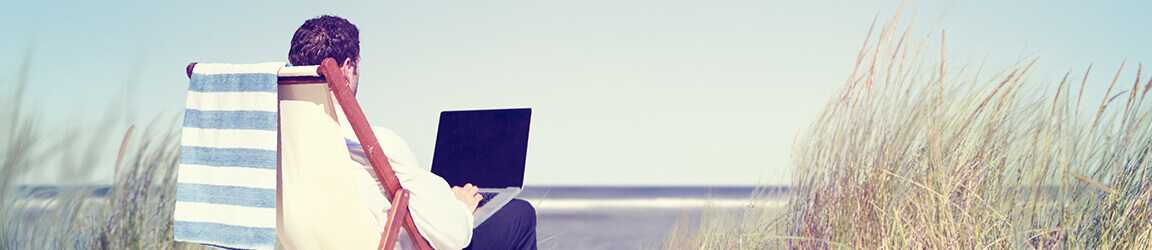 Business man sitting on lounge chair while using laptop on the beach